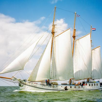 Traditionelles Segelschiff Elizabeth mit voll entfalteten weißen Segeln, segelnd auf grün-blauem Wasser unter teilweise bewölktem Himmel mit niederländischer Flagge.