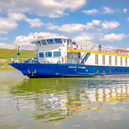 Flusskreuzfahrtschiff MS Prinzessin Katharina mit blauem Rumpf und weißem Aufbau fährt auf der Donau unter teilweise bewölktem Himmel.