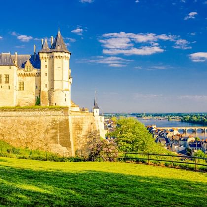 Château de Saumur, ein weißes mittelalterliches Schloss mit Türmen, auf einem Hügel mit Blick auf die Loire und die Stadt Saumur mit Brücke.