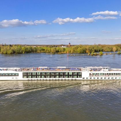 Weißes Flusskreuzfahrtschiff MS Lisabelle auf der Donau mit grünem bewaldeten Ufer und blauem Himmel im Hintergrund.
