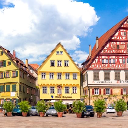 Panoramablick auf den Esslinger Marktplatz mit bunten Fachwerkhäusern, Kirchturm und parkenden Autos unter blauem Himmel mit Wolken.