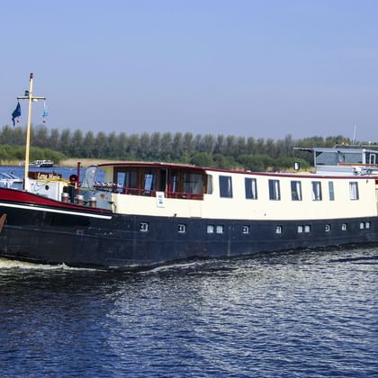 MS Lena Maria, ein Passagierschiff mit dunkelblauem Rumpf und weißem Aufbau, fährt auf einem Fluss mit Bäumen am Ufer.