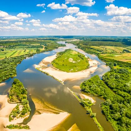 Luftaufnahme der Weichsel, die sich durch grüne Felder und Wälder in Polen schlängelt, unter blauem Himmel mit weißen Wolken.