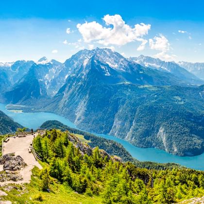 Luftaufnahme des Königssees umgeben von steilen Bergen in Oberbayern. Türkisfarbenes Wasser schlängelt sich zwischen bewaldeten Hängen.