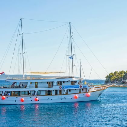 Weiße Motoryacht MS Amore mit zwei Masten und roten Fendern in ruhigen blauen kroatischen Gewässern, mit bewaldeter Küste im Hintergrund.