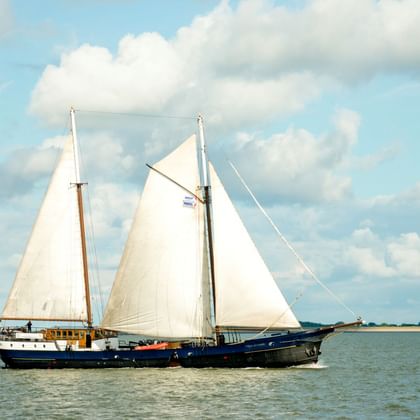 Traditionelles niederländisches Segelschiff Wapen fan Fryslân mit dunkelblauem Rumpf und weißen Segeln auf ruhigem Wasser unter bewölktem Himmel.