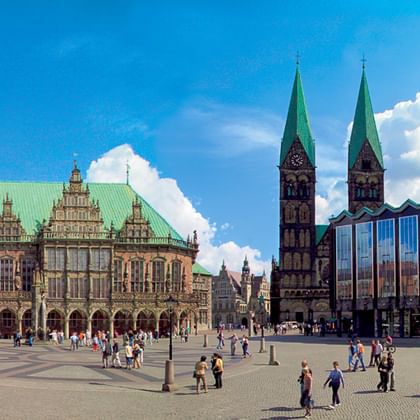 Bremen Market Square with historic Town Hall featuring green copper roof, twin-spired cathedral, and modern glass building under blue sky.