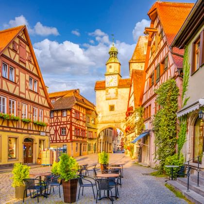 Historische Straße in Rothenburg ob der Tauber mit bunten Fachwerkhäusern, Markusturm mit grüner Spitze und Röderbogen.