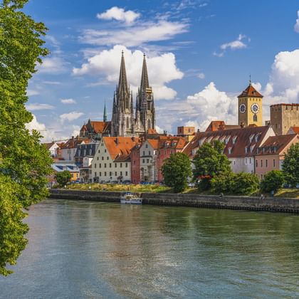 Regensburger Altstadt mit Domtürmen und mittelalterlichen Türmen an der Donau unter blauem Himmel mit weißen Wolken.