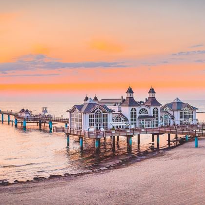 Historische Seebrücke Sellin mit weißem Pavillon auf Holzpfählen, die bei Sonnenuntergang in die Ostsee ragt.
