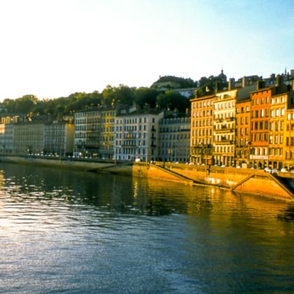 Blick auf die Rhône in Lyon mit farbenfrohen historischen Gebäuden entlang des Ufers, die von goldenem Sonnenlicht beleuchtet werden.