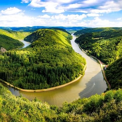 Luftaufnahme der Saarschleife, einer dramatischen Flussschleife der Saar, umgeben von dicht bewaldeten Hügeln unter blauem Himmel.