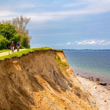 Zwei Radfahrer auf einem Weg an der Brodtner Steilküste bei Travemünde, mit steilen Küstenklippen und Ostsee.