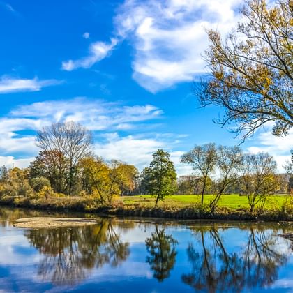 Calm river with perfect reflections of trees and blue sky in Bavaria. Green meadows and autumn trees line the riverbank along the Five Rivers Route.