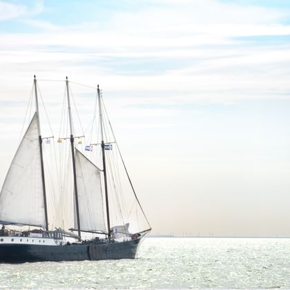 Dreimaster-Segelschiff mit weißen Segeln auf ruhigen Gewässern des Mare fan Fryslân unter bewölktem Himmel in den Niederlanden.
