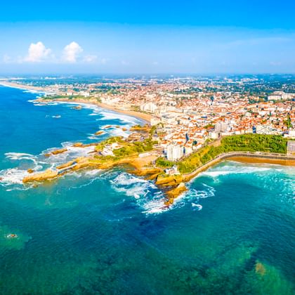 Luftaufnahme von Biarritz, Frankreich mit Atlantikküste, felsigen Klippen, Stränden und der Stadt unter blauem Himmel.