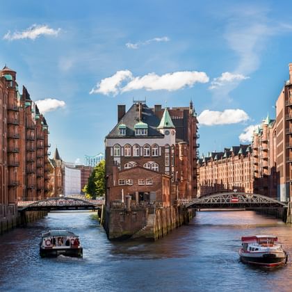 Kanal in der Hamburger Speicherstadt mit roten Backsteinspeichern auf beiden Seiten, zwei Brücken und Ausflugsbooten auf dem Wasser.