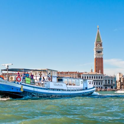 Blaues Kreuzfahrtschiff MS Vita Pugna in der Lagune von Venedig mit Markusturm und historischen Gebäuden im Hintergrund.