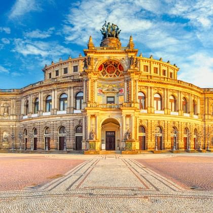 The Semperoper opera house in Dresden with its ornate Neo-Renaissance facade in golden sunlight, featuring arched windows and sculptures on top.