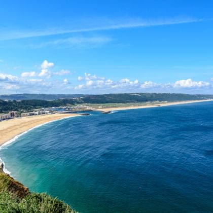 Panoramablick auf einen langen Sandstrand und blaues Meer entlang der portugiesischen Küste zwischen Porto und Lissabon unter hellem Himmel.