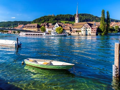 Historische Stadt Stein am Rhein mit bunten Gebäuden, Kirchturm und Booten auf dem Rhein unter blauem Himmel.