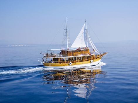 Traditionelles Holzsegelschiff MS Planka mit weißen Segeln auf ruhigem blauen Adriatischen Meer mit sichtbarer Küstenlinie.