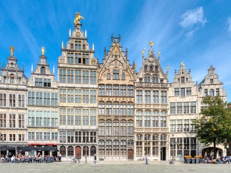 Reihe prächtiger Gildehäuser mit Treppengiebeln und goldenen Statuen in Antwerpen. Menschen entspannen auf dem Kopfsteinpflasterplatz.