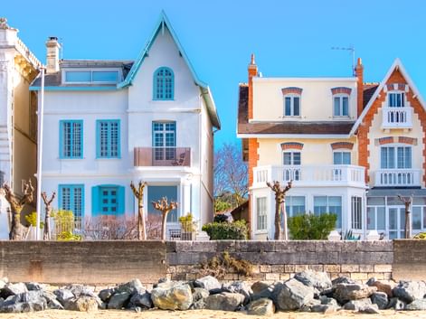 Reihe bunter Strandhäuser in Royan mit weißen und türkisfarbenen Fassaden und markanter Architektur. Felsiger Strand im Vordergrund.