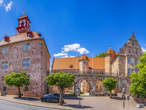 Landgrafenschloss Eschwege mit roten Sandsteingebäuden, Glockenturm und orangen Ziegeldächern. Bäume säumen den Kopfsteinpflasterhof unter blauem Himmel.