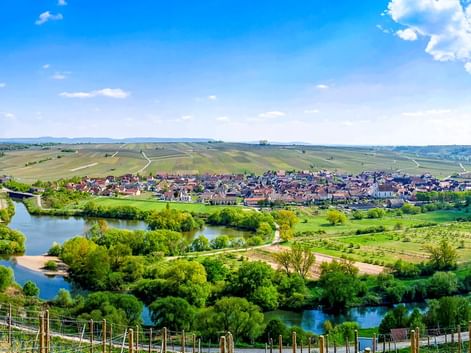Panoramablick auf die Volkacher Mainschleife mit dem Main, der sich durch grüne Weinberge und Felder schlängelt, mit der Stadt Volkach in der Mitte.