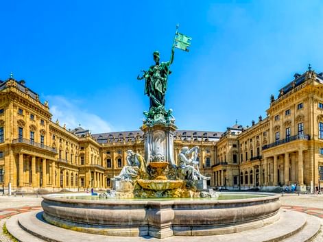 Panoramablick auf die Würzburger Residenz, ein prächtiger Barockpalast mit gelber Fassade und prunkvollem Brunnen im Innenhof.
