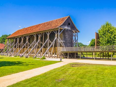 Historisches Salzlagerhaus Saline Gottesgabe in Rheine mit markanten diagonalen Holzstützen und orangefarbenem Ziegeldach auf grüner Wiese.