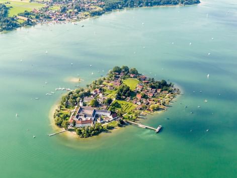 Luftaufnahme der Fraueninsel, einer kleinen Insel im bayerischen Chiemsee mit historischen Gebäuden, grünen Wiesen und Bäumen, umgeben von türkisfarbenem Wasser.