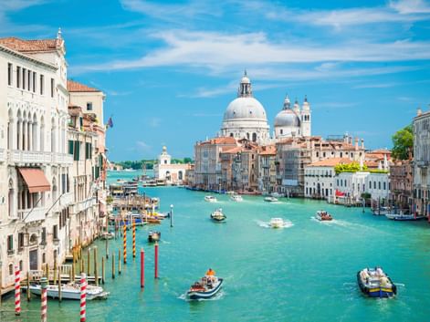 Venedigs Canal Grande mit türkisfarbenem Wasser, Booten und bunten Gebäuden. Die weiße Kuppelbasilika Santa Maria della Salute dominiert den Hintergrund.