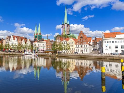 Historische Lübecker Altstadt am Wasser mit bunten Gebäuden und Kirchtürmen, die sich im ruhigen Wasser unter blauem Himmel spiegeln.