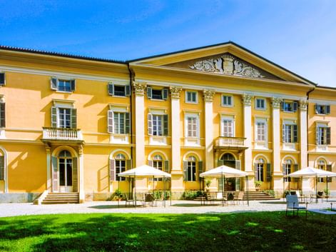 Gelbe neoklassizistische Villa Matilde mit weißen Säulen und dekorativem Giebel in Romano Canavese. Terrasse mit weißen Sonnenschirmen.
