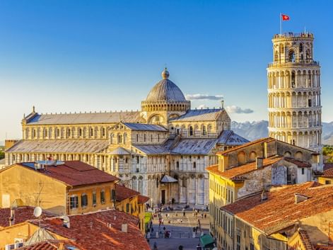 Luftaufnahme des Domplatzes von Pisa mit dem Schiefen Turm, dem Dom mit Kuppel und umliegenden historischen Gebäuden mit Terrakottadächern.
