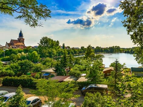 Blick auf Waren mit St. Marien Kirchturm und Tiefwarensee, eingerahmt von grünen Bäumen. Boote und Gebäude am Ufer sichtbar.