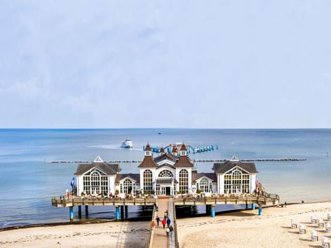 Historische Seebrücke Sellin in der Ostsee mit weißem Pavillongebäude, Sandstrand mit Strandkörben und ruhigem blauem Wasser.