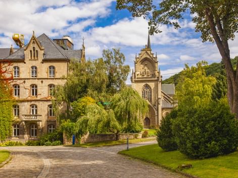 Historisches Zisterzienserkloster Schulpforte mit Kirchturm und Wohngebäuden, umgeben von grünen Rasenflächen und Bäumen unter blauem Himmel.