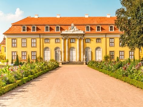 Yellow baroque palace with orange roof and white columns in Mosigkau near Dessau. A gravel path leads through a formal garden to the entrance.