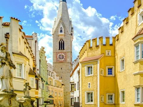 Bunte mittelalterliche Gebäude mit Zinnen säumen eine enge Gasse in Brixens Altstadt, mit einem weißen Kirchturm in der Mitte.