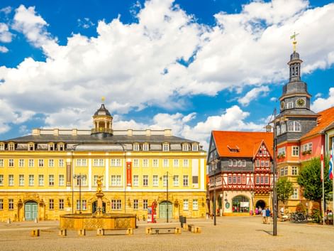 Marktplatz in Eisenach mit gelbem Rathaus, Fachwerkhäusern und Kirchturm mit Uhr unter blauem Himmel mit weißen Wolken.