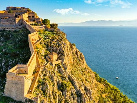 Festung Palamidi in Nafplio auf einer steilen Klippe mit Blick auf das blaue Meer. Steinbefestigungen schlängeln sich den felsigen Hang hinunter.