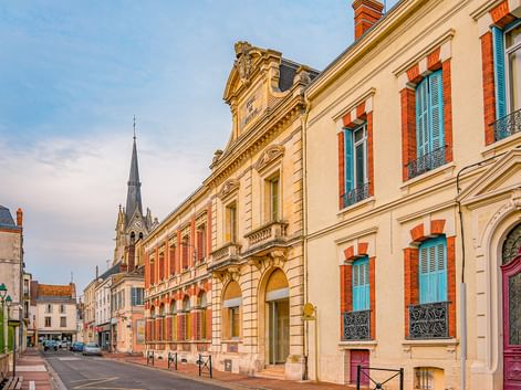 Straßenansicht der Altstadt von Montargis mit farbenfrohen historischen Gebäuden mit türkisfarbenen Fensterläden, verzierten Fassaden und Kirchturm.