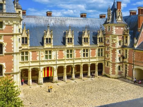 Kopfsteinpflaster-Innenhof des Château de Blois mit Renaissance-Architektur, verzierten Dachgauben und Arkadengang unter blauem Himmel.