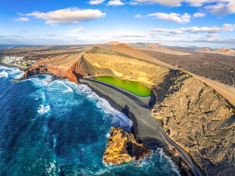 Aerial view of El Golfo's bright green lagoon surrounded by volcanic crater, black sand beach, and turquoise ocean on Lanzarote, Spain.