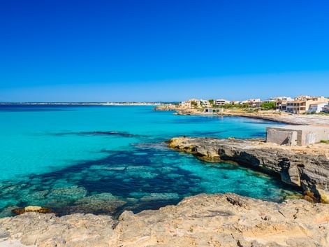 Türkisfarbene Mittelmeerbucht mit felsiger Kalksteinküste und weißen Gebäuden im Hintergrund unter klarem blauen Himmel in Spanien.