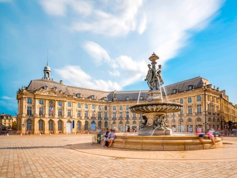Place de la Bourse in Bordeaux mit prächtigem Brunnen in der Mitte des Kopfsteinpflasterplatzes, umgeben von klassischen Gebäuden aus dem 18. Jahrhundert.