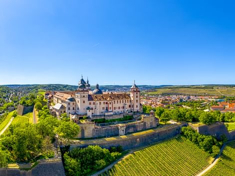 Luftaufnahme der Festung Marienberg in Würzburg, umgeben von Weinbergen und Festungsmauern, mit Blick auf die Stadt und das Flusstal.